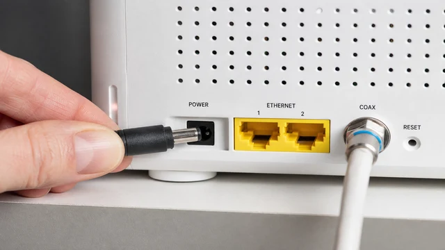 Hand unplugging power cord from white cable modem